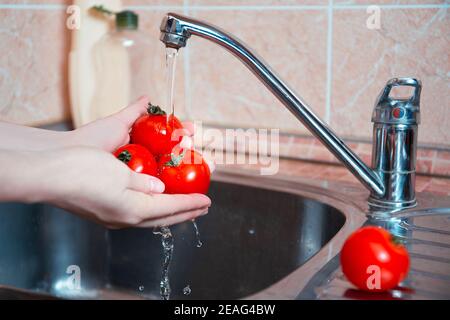 Une femme lave trois tomates juteuses sous l'eau courante dans la cuisine avant de cuisiner. Hygiène, soins de santé, soins familiaux. Protection contre les germes, vi Banque D'Images