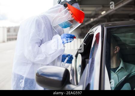 Travailleur médical dans l'EPI portant un écouvillon nasal et de gorge Personne dans le véhicule à travers la fenêtre de voiture, centre d'essai mobile COVID-19, conduire à travers par. de l'installation Banque D'Images