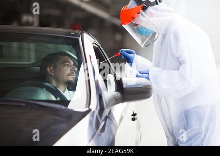 Site de détection de rt-PCR au drive-in COVID-19, travailleur médical réalisant un échantillon d'écouvillon nasal Collection sur jeune homme conducteur, gratuit coronavirus public diagno Banque D'Images