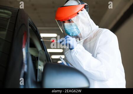 Travailleur médical dans un équipement de protection individuelle qui a fait des coups de couteau dans une personne Une voiture traverse le centre de test mobile coronavirus COVID-19, oral et spe nasale Banque D'Images