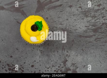 Vue de dessus d'un cupcake blanc et brun jaune givré sur fond gris marbré. Banque D'Images