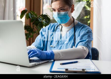 Jeune femme caucasienne médecin travaillant sur ordinateur portable dans le bureau, portant Gant de protection et masque facial, Electronic Medical Records concept EMR Banque D'Images