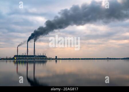 Centrale à charbon haute tuyauterie avec fumée noire se déplaçant vers le haut atmosphère polluante avec des réflexions de lui dans l'eau du lac. Banque D'Images