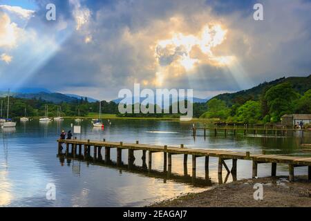 Le soleil traverse des nuages et une jetée en bois sur le lac Windermere, dans le district des lacs anglais, vu à Waterhead à Ambleside, Cumbria, au nord-ouest de l'Angleterre Banque D'Images