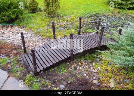 Un petit pont en bois brun dans le jardin. Un pont sur un ruisseau en pierres. Banque D'Images