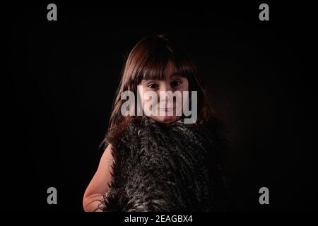 Élégante jeune fille de quatre ans de race blanche vêtue d'un gilet en plumes avec un portrait d'expression adorable et attachant regardant l'appareil photo Banque D'Images