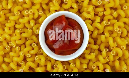 Soucoupe avec de délicieux ketchup rouge sur fond de nombreuses pâtes sèches sous forme de spirales. Mise au point sélective. La nourriture. Vue de dessus. Gros plan. Banque D'Images
