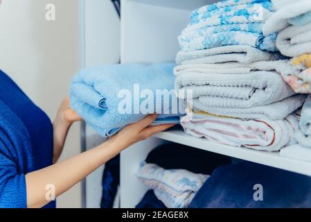 Femme mains tenant les serviettes et les mettant sur une étagère sur le tiroir de l'armoire lors du nettoyage général par le système de stockage moderne. Concept de confort Banque D'Images