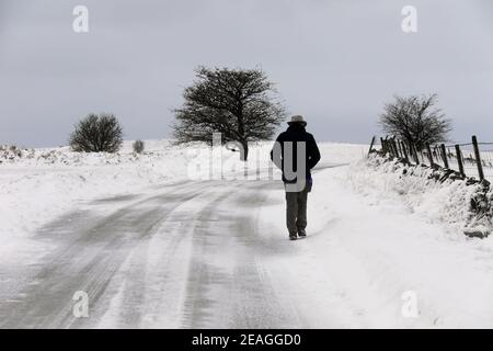 Homme marchant le long de la route enneigée à Longstone Moor Près de Bakewell dans le Peak District Banque D'Images