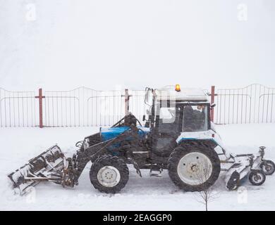 Le tracteur roule sur la route et élimine la neige pendant un blizzard. Banque D'Images