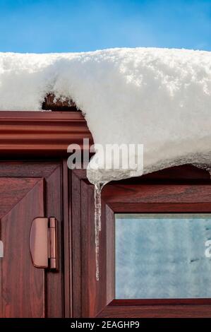 Neige slumpimg d'un toit et formant des glaçons, contre un ciel bleu. Pendant l'hiver 2021. Banque D'Images