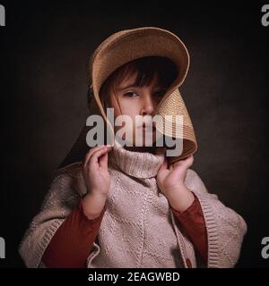 Fille caucasienne de 4 ans avec chapeau et poncho en tissu. Elle pose élégante et élégante en tenant le chapeau avec ses mains. Banque D'Images