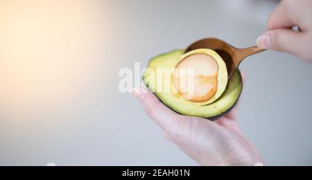 Main femelle à l'aide d'une cuillère pour retirer l'avocat de la coquille et préparer la cuisine, pour le concept de fruits et légumes frais. Banque D'Images