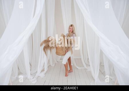 Jeune femme blonde dans une chemise lilas, robe blanche, tient dans ses mains panier de paille avec l'herbe de pampas parmi les aérées, développant des tissus de tulle. Minimali Banque D'Images