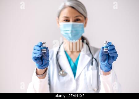 Une travailleuse médicale défocused, portant un masque médical, tient dans les mains et les ampoules avec un vaccin coronavirus, covid19. Concept de vaccination et de soins de santé Banque D'Images