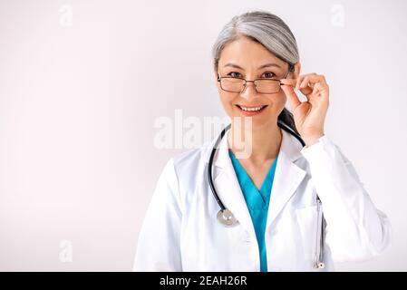 Portrait en gros plan de la femme cacasienne attrayante médecin en uniforme médical et stéthoscope se tient contre un fond blanc, regarde l'appareil photo et sourit. Concept de soins de santé Banque D'Images