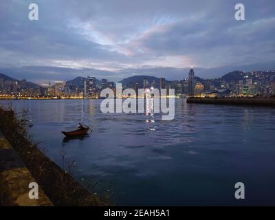 Le bateau de pêche rustique dans le port Victoria de Hong Kong contraste avec l'horizon moderne de l'île de Hong Kong au début de l'aube Banque D'Images