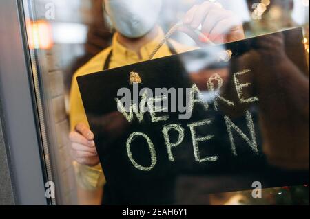 Photo en gros plan d'un panneau OUVERT à l'entrée d'un restaurant ou d'un café. Une main masculine tient une affiche OUVERTE à l'entrée d'un restaurant, d'un bar, d'un café ou d'une boutique Banque D'Images