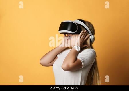 Jeune femme blonde en t-shirt blanc et lunettes VR est émerveillé par la technologie moderne de réalité virtuelle augmentée Banque D'Images