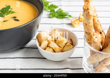 Un bol de soupe de potiron biologique crémeuse épicée maison sur fond de tissu blanc rayé avec des bâtonnets de pain, de la crème sure, du persil et des épices. Wi Banque D'Images