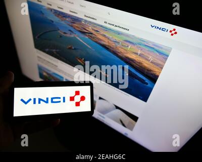 Personne tenant un smartphone avec le logo de la société française de concessions et de construction Vinci S.A. à l'écran devant le site. Mise au point sur l'affichage du téléphone. Banque D'Images