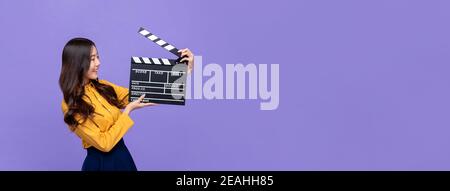 Jeune belle fille asiatique tenant un film clapperboard isolé sur violet arrière-plan de bannière avec espace de copie Banque D'Images