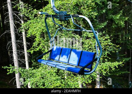 Un gros plan de chaise sur la remontée mécanique dans les montagnes et la forêt. Téléphérique siège vide parmi les arbres, champ d'herbe dans la forêt verte sur la colline, été ensoleillé Banque D'Images