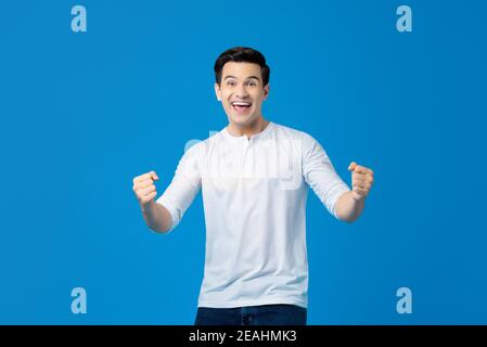 Heureux excité jeune homme caucasien élevant ses poings faisant oui geste célébrant le succès isolé sur fond bleu Banque D'Images