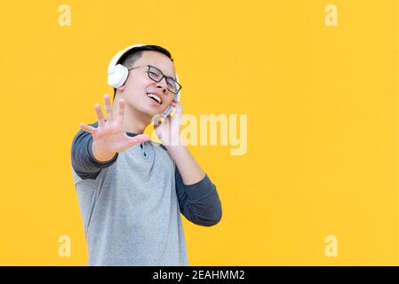 Jeune homme asiatique portant un casque pour écouter de la musique et faire des choses mouvement d'arrêt isolé sur fond jaune Banque D'Images