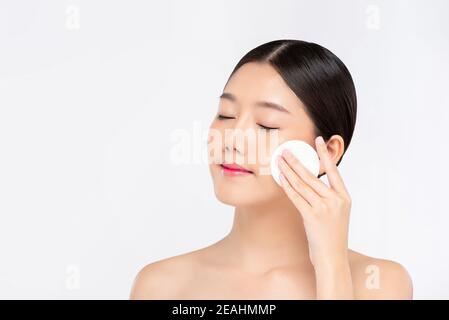 Belle femme asiatique nettoyant délicatement le visage avec un tampon démaquillant isolé sur fond blanc Banque D'Images