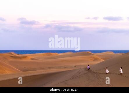 Gran Canaria, Espagne. 5 octobre 2020. Trois femmes portant des robes blanches marchant à travers les dunes de Maspalomas au coucher du soleil avec bleu océan et ciel violet en t Banque D'Images