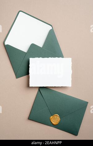 Maquette de carte d'invitation de mariage et enveloppes vertes sur fond marron. Flat lay, vue de dessus, espace de copie. Banque D'Images