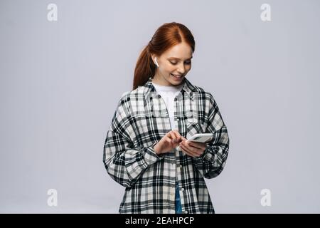 Photo de jeune femme gaie à tête rouge utilisant la technologie moderne écouteurs oreilles écouter la chanson populaire. Banque D'Images