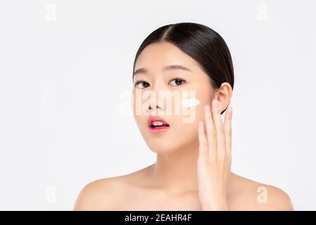 Jeune belle femme asiatique avec une apparence propre fraîche application de crème au visage isolé sur fond blanc pour les concepts de beauté et de soins de la peau Banque D'Images