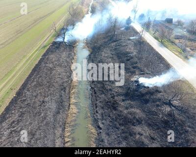 La combustion de l'herbe sèche le long du canal d'irrigation. La fumée et la flamme de l'herbe sèche. Brûlé de l'herbe sèche. Banque D'Images