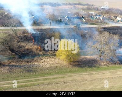 La combustion de l'herbe sèche le long du canal d'irrigation. La fumée et la flamme de l'herbe sèche. Brûlé de l'herbe sèche. Banque D'Images