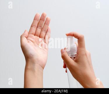 Mains d'une femme utilisant un spray désinfectant sur fond gris Banque D'Images