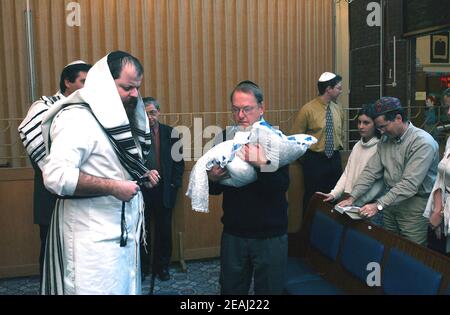 Une cérémonie de Brit Mila a lieu sur la bimah de la synagogue dans le Solihull, West Midlands, comme le Mohel donne les bénédictions traditionnelles comme il commence la circoncision surveillée par le rabbin et les membres de la famille. Banque D'Images