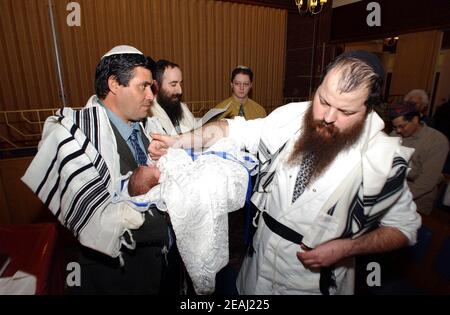 Une cérémonie de Brit Mila a lieu sur la bimah de la synagogue dans le Solihull, West Midlands, comme le Mohel donne les bénédictions traditionnelles comme il commence la circoncision surveillée par le rabbin et les membres de la famille. Banque D'Images