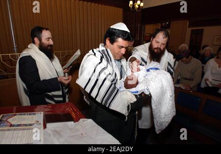 Une cérémonie de Brit Mila a lieu sur la bimah de la synagogue dans le Solihull, West Midlands, comme le Mohel donne les bénédictions traditionnelles comme il commence la circoncision surveillée par le rabbin et les membres de la famille. Banque D'Images