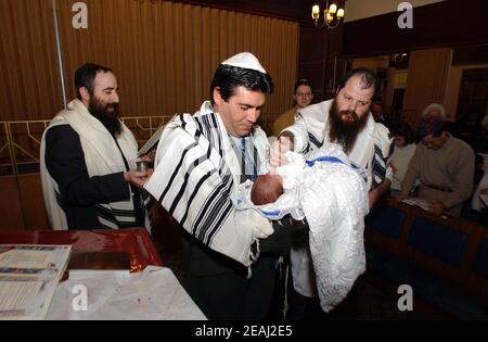 Une cérémonie de Brit Mila a lieu sur la bimah de la synagogue dans le Solihull, West Midlands, comme le Mohel donne les bénédictions traditionnelles comme il commence la circoncision surveillée par le rabbin et les membres de la famille. Banque D'Images