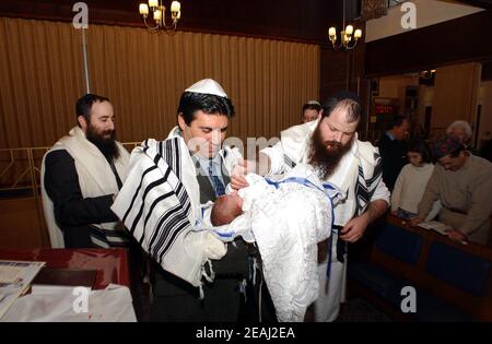 Une cérémonie de Brit Mila a lieu sur la bimah de la synagogue dans le Solihull, West Midlands, comme le Mohel donne les bénédictions traditionnelles comme il commence la circoncision surveillée par le rabbin et les membres de la famille. Banque D'Images