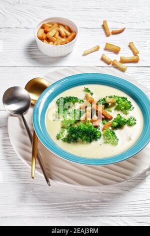 soupe à la crème avec brocoli et croûtons dans un bol bleu sur une table blanche en bois avec des cuillères , vue verticale d'en haut Banque D'Images