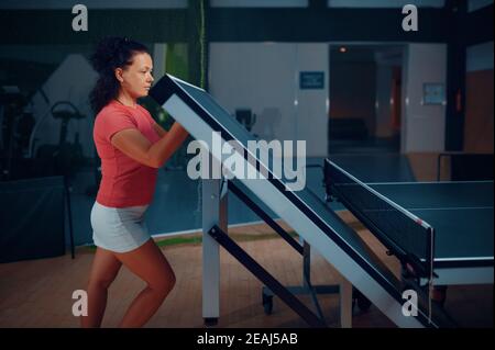 Une femme plie une table de ping-pong, fait de l'exercice de tennis Banque D'Images