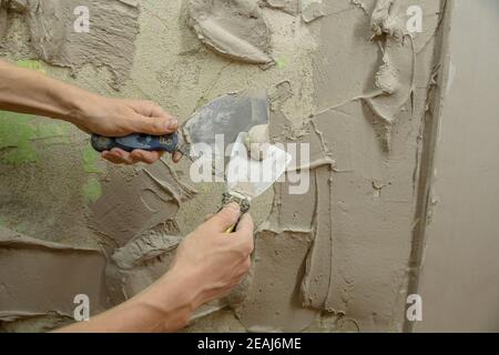 Un ouvrier plâtres le mur avec une spatule et applique une solution de mélange de ciment. Le réparateur pose le plâtre sur la cloison sèche. Le handyman répare à la maison. Restauration de l'habitation par un ouvrier. Un spécialiste couvre les fissures Banque D'Images