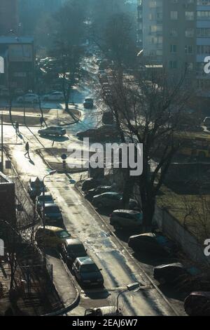 Matin brumeux ensoleillé, une vue de la fenêtre sur les bâtiments de la ville, la rue, les gens. Voitures garées dans la cour d'un immeuble. Photo verticale. Banque D'Images