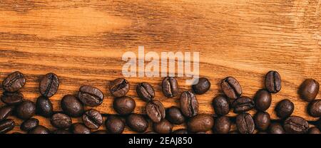 Gros plan de grains de café éparpillés sur une table en bois texturé. Banque D'Images