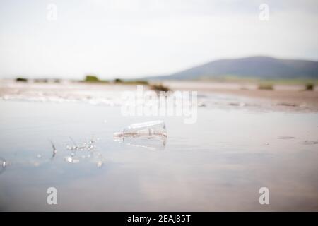 Flacons en plastique avec litière flottant dans une flaque au milieu Du sable Banque D'Images