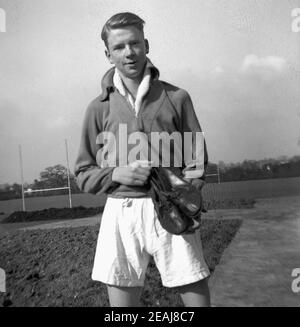 1956, historique, debout à l'extérieur d'un terrain de sport, un jeune homme dans son équipement sportif et tenant une paire de chaussures de course ou de chaussures de course, des chaussures spéciales pour courir sur des pistes de sport de cinder d'extérieur. C'était le moment où le grand Roger Banister, un amateur, un étudiant-athlète, a brisé le 4 minute mile à une telle piste à l'Université d'Oxford en 1954. Banque D'Images