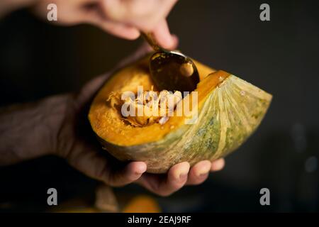 Les mains de l'homme retirent les graines d'une citrouille ronde fraîchement coupée avec un fond noir. Le style sombre de l'éclairage doux est idéal pour Halloween et l'automne. Clos Banque D'Images